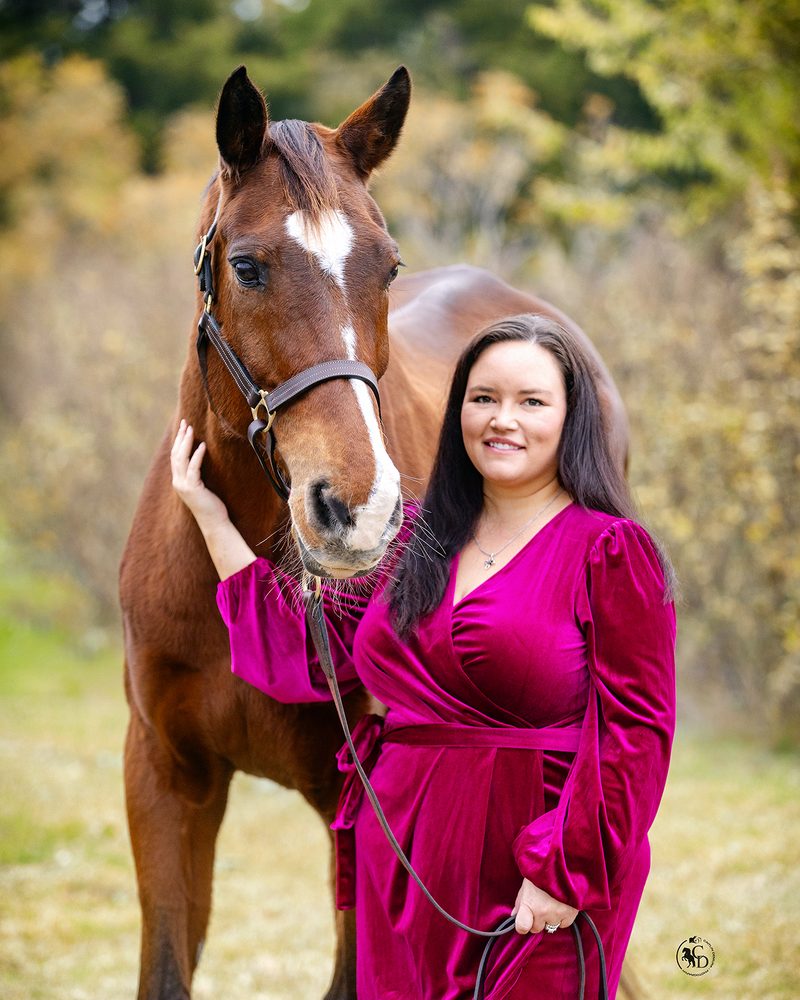 Jessica Hart smiling beside her chestnut horse, with autumn trees behind them